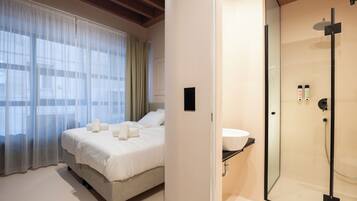 A hotel room with a bed, a shower, and a window with curtains.