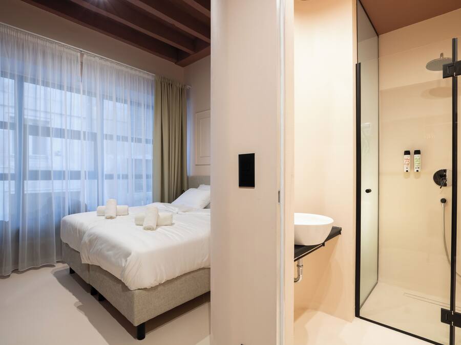A hotel room with a bed, a shower, and a window with curtains.