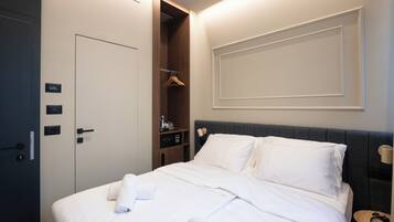 A hotel room with a bed, a wardrobe, a shelf with toiletries, and a bedside table with a lamp.
