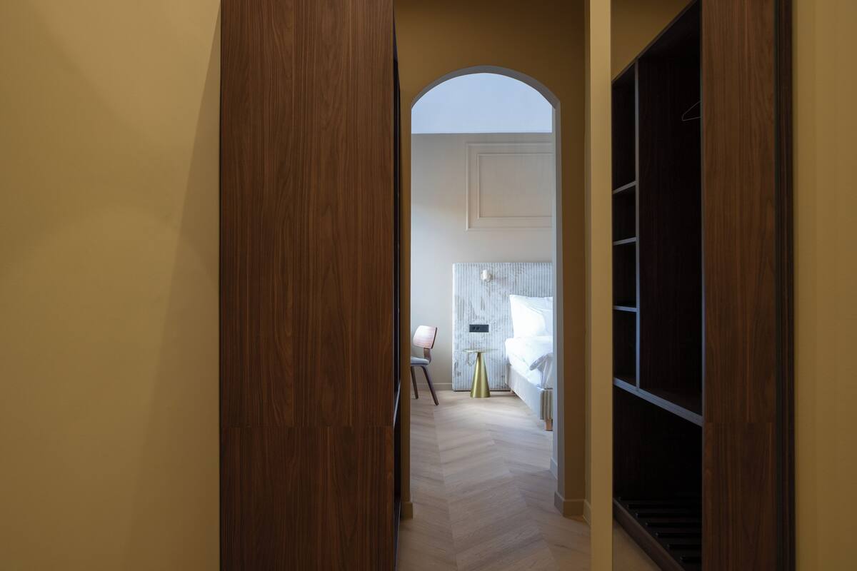 Un couloir menant à une chambre à coucher qui contient un lit, une chaise et une petite table.