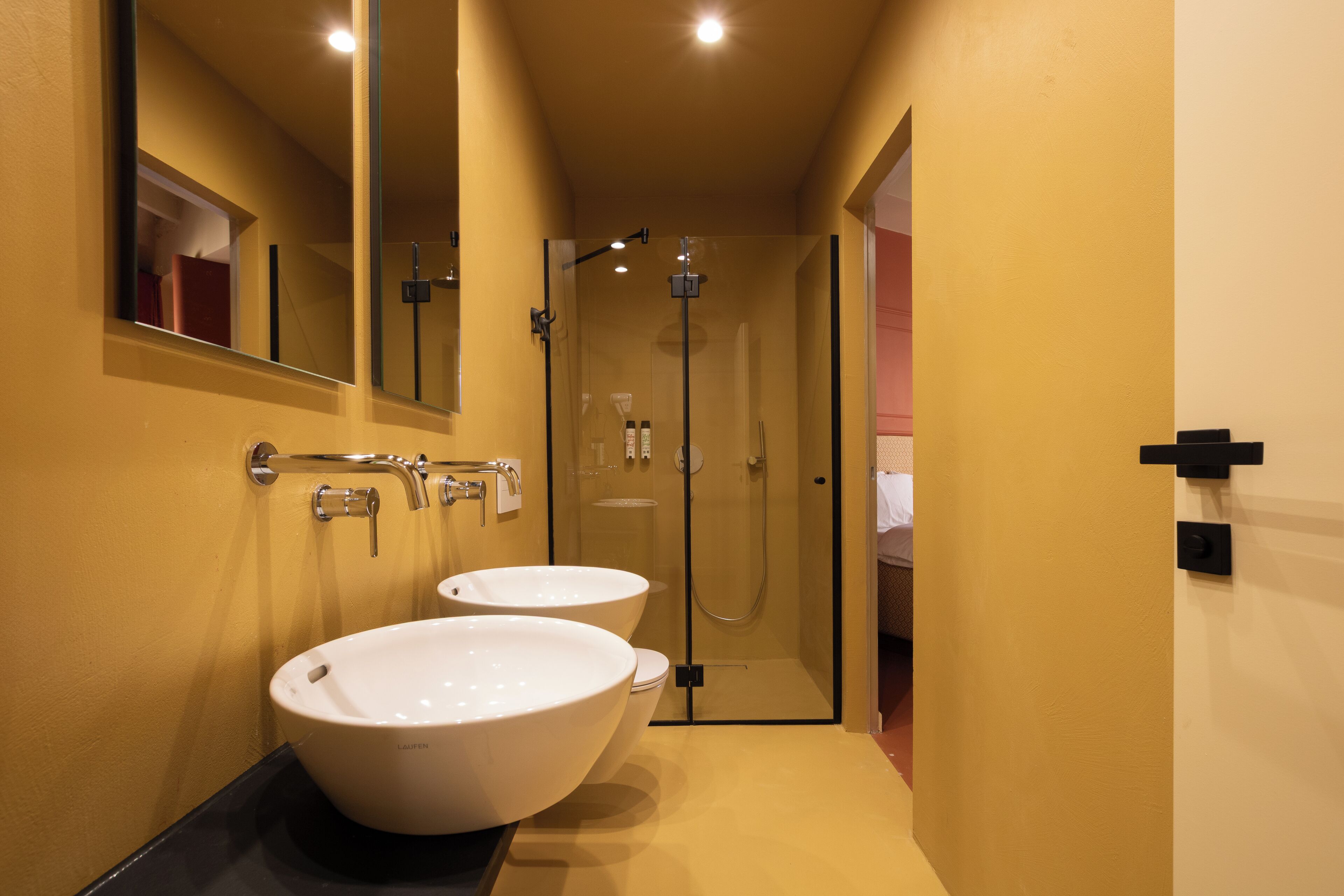 A modern bathroom with two white sinks, a glass-enclosed shower, and a mirror above the sinks.