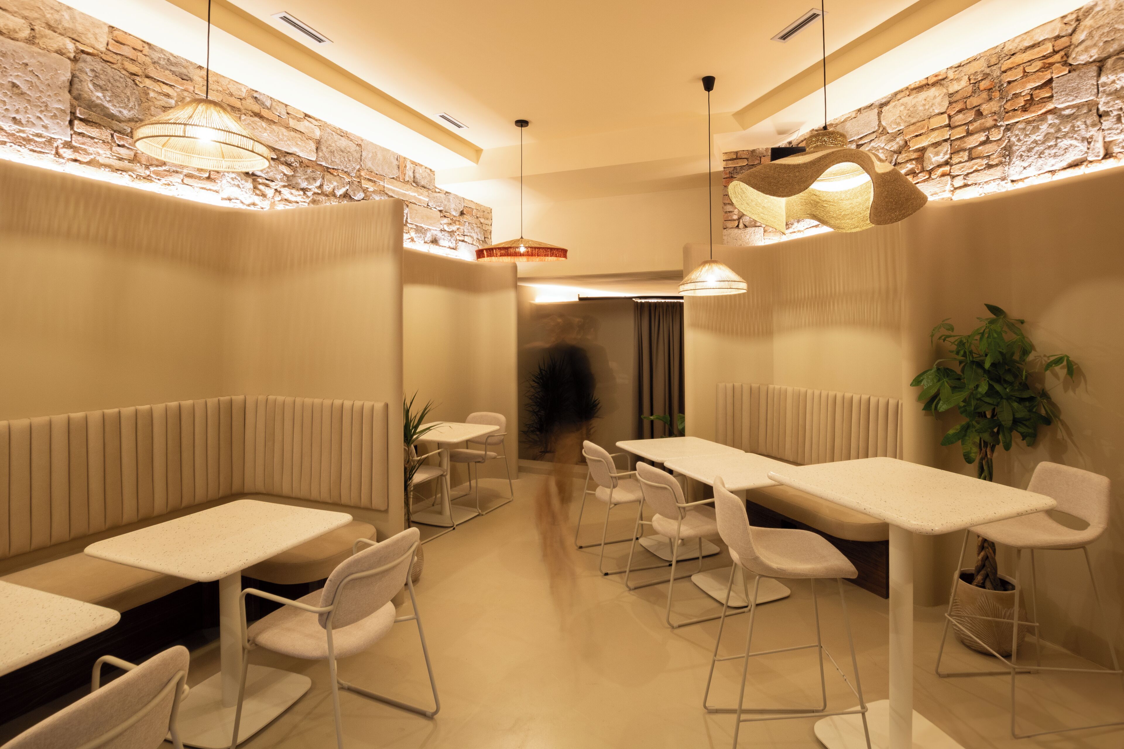 A modern dining area with white tables and chairs, a stone accent wall, and hanging pendant lights.