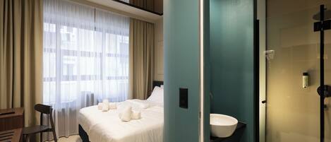 A hotel room with a bed, a desk, a chair, a bathroom with a sink, and a shower.