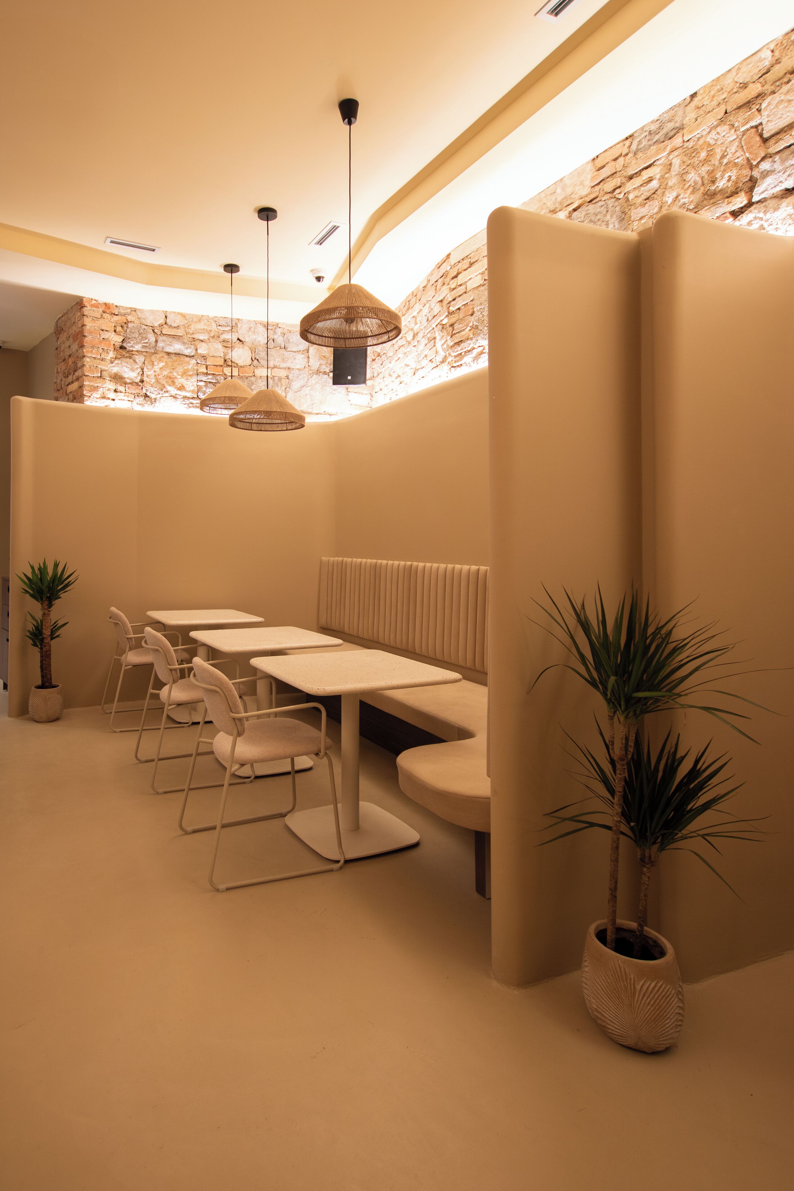 Een modern interieur met een stenen muur, een zithoek met tafels en stoelen, en hangende pendantlampen.