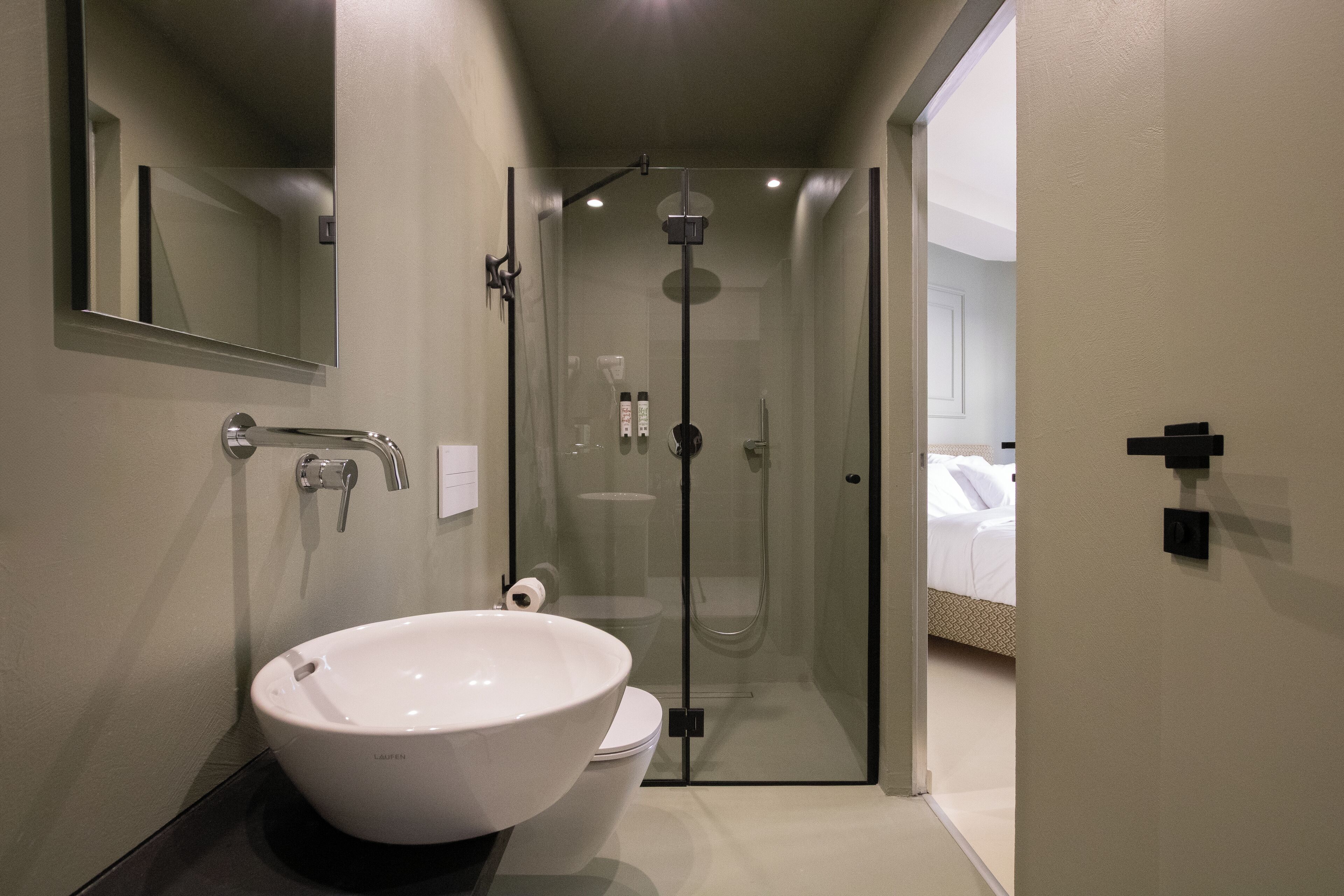 A modern bathroom with a large white sink, a toilet, and a glass-enclosed shower.