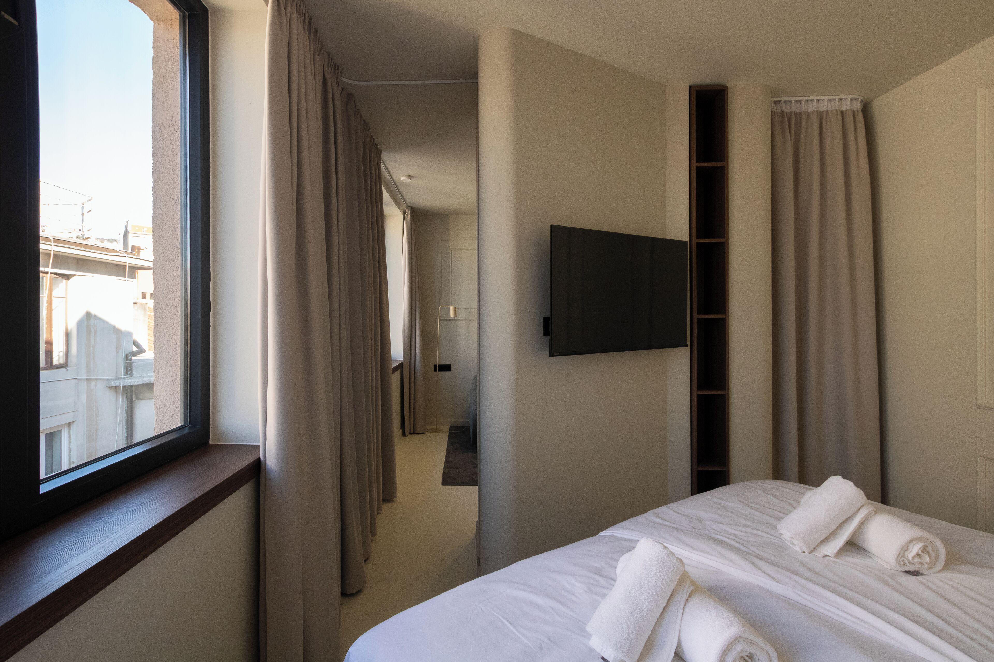 A hotel room with a bed, a TV mounted on the wall, and a window with curtains.