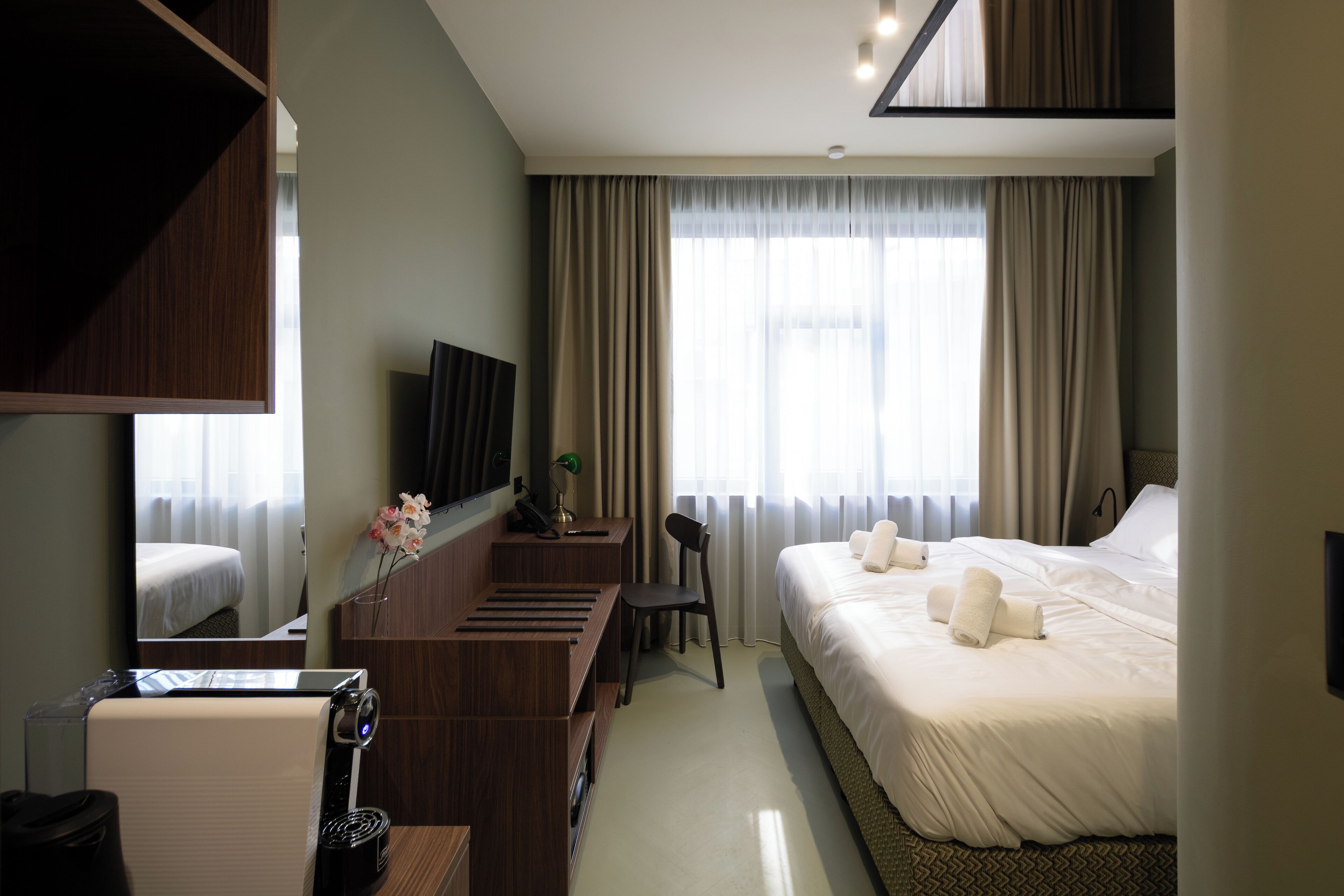 Una habitación de hotel con cama, escritorio con computadora, silla, televisión y ventana con cortinas.