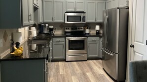 A modern kitchen with grey cabinets, stainless steel appliances, and a black countertop. - Designer Furnished Home Away from Home (Horseshoe Bay)