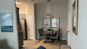 A dining area with a table, chairs, and a bench. There is a refrigerator and a door in the background. - Designer Furnished Home Away from Home (Horseshoe Bay)
