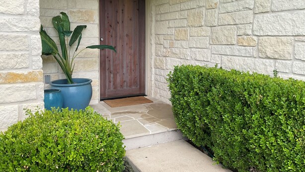 A stone building with a wooden door, a potted plant, and trimmed hedges. - Designer Furnished Home Away from Home (Horseshoe Bay)