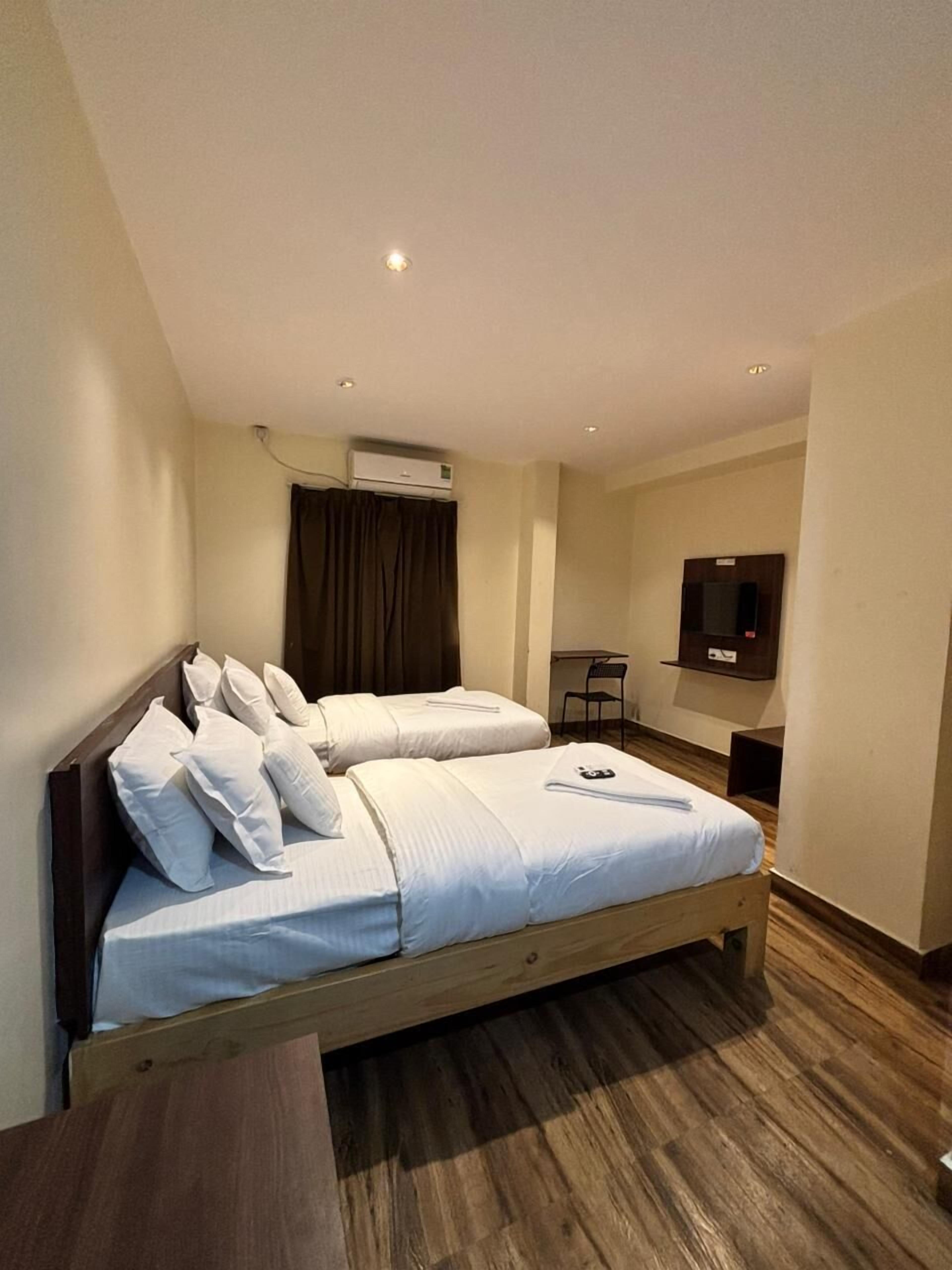 A double bed with white linens, a wooden headboard, a small desk with a chair, and a mounted TV on the wall.