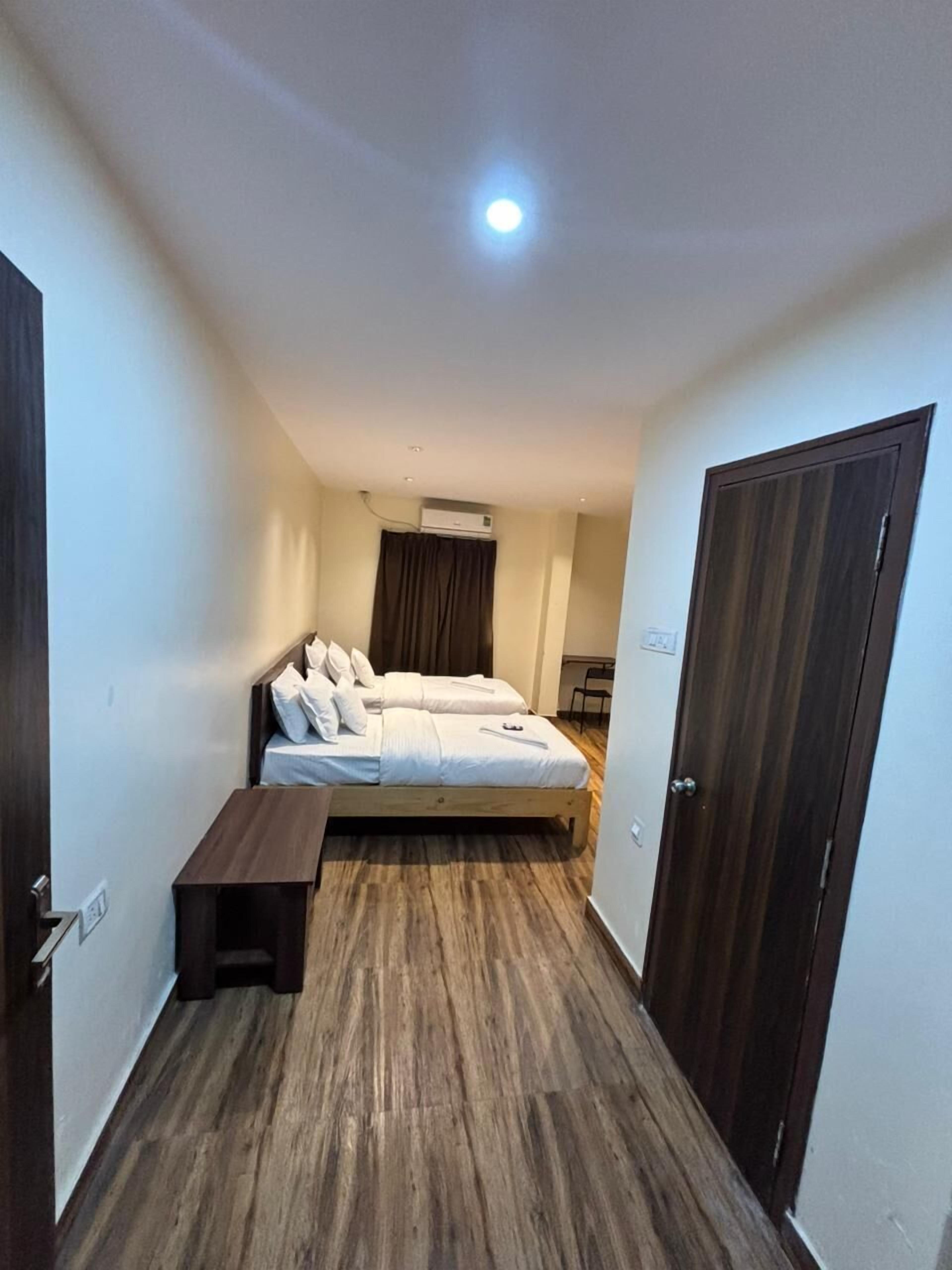 Un pasillo estrecho que conduce a una cama con cabecera, una mesita de noche y una puerta.