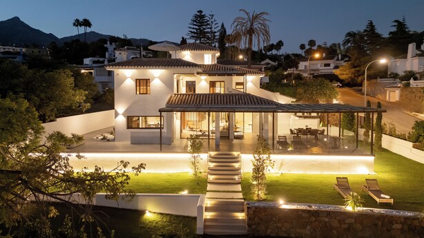 Ein modernes, zweistöckiges Haus mit einer überdachten Terrasse, einem Schwimmbad und einem gut beleuchteten Garten.