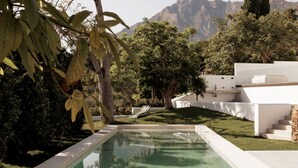 Ein moderner Poolbereich mit freiem Blick auf die dahinterliegenden Berge, umgeben von üppiger Vegetation und weißen architektonischen Elementen.