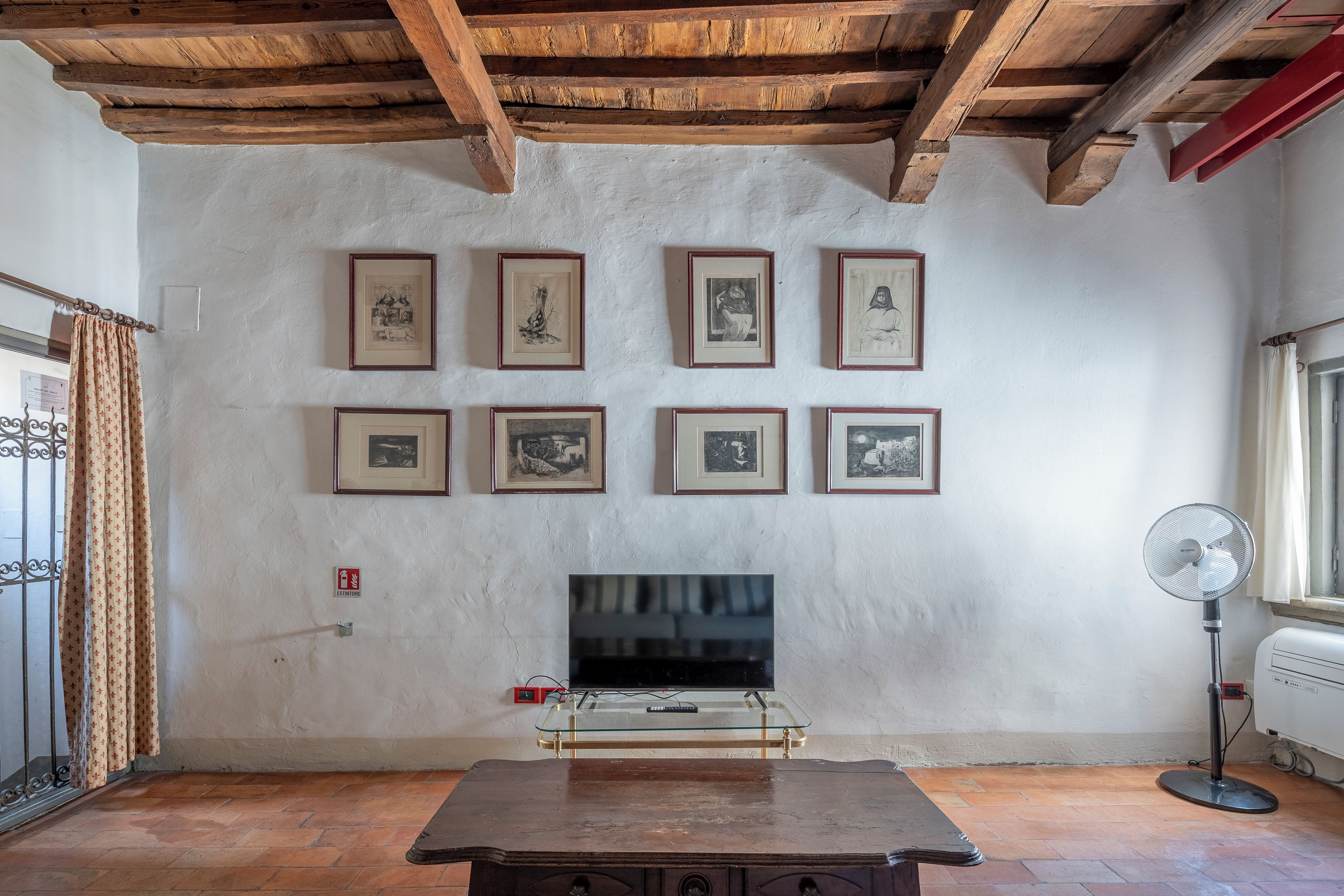 Un salon avec un plafond en bois, un téléviseur posé sur un meuble en verre et des tableaux encadrés accrochés au mur.
