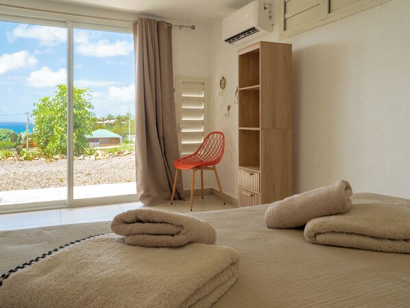 A hotel room with a large window, a wooden wardrobe, a red chair, and towels on the bed. - Villa Joséphine, unbeatable ocean view, luxury villa with private pool. (Grand-Bourg)