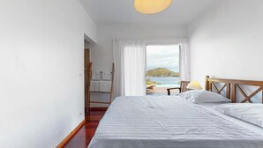 Een slaapkamer met een bed, een houten hoofdbord, een raam met uitzicht op zee en een houten ladder die tegen de muur staat.