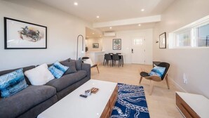 A modern living room with a grey sofa, a coffee table, and a patterned rug. There is a dining area with a table and chairs in the background. - Entire 2 Unit Duplex, King Beds, Rock View EV (Morro Bay)