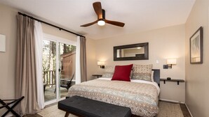 Quarto com cama, ventoinha no teto, um banco, porta de correr de vidro e vista para o exterior.