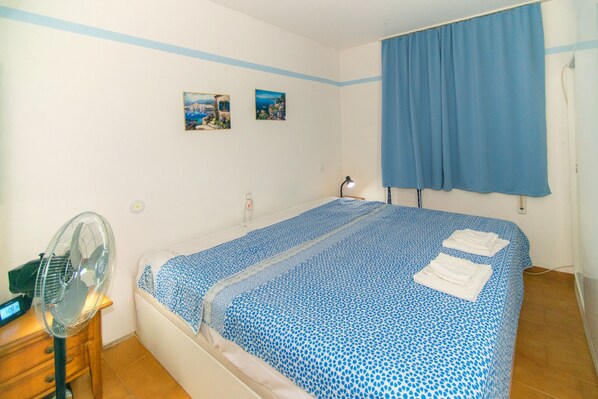 Una camera da letto con un letto, un comodino, una ventola e due quadri appesi al muro.