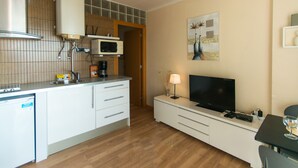 A modern kitchen with a microwave, stove, and dishwasher. There is a dining area with a table and chairs, and a television on a stand. - WELCS STUDIO 294 EMP with sea view (Empuriabrava)
