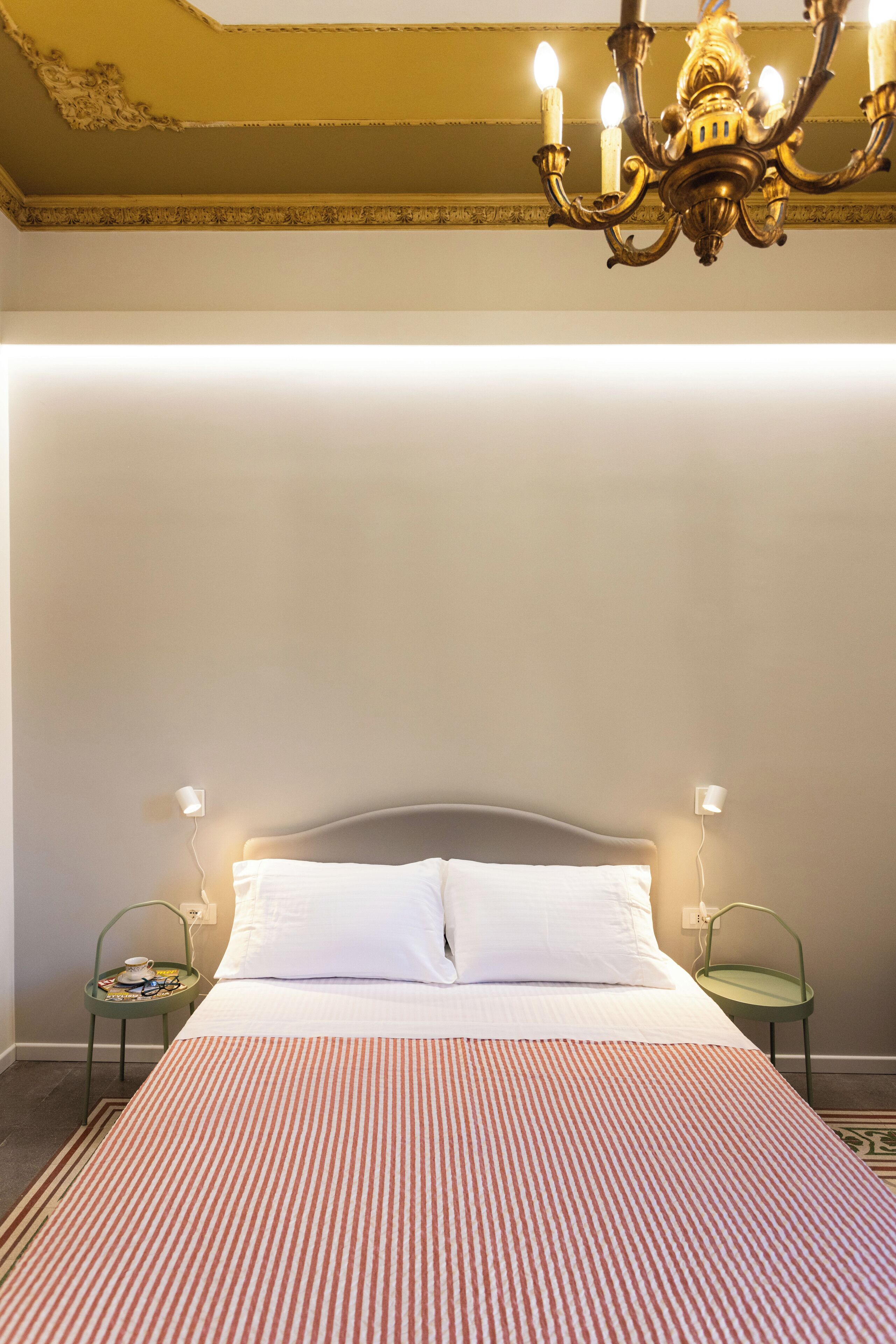 A hotel room with a large bed, a chandelier, and two bedside tables with lamps.
