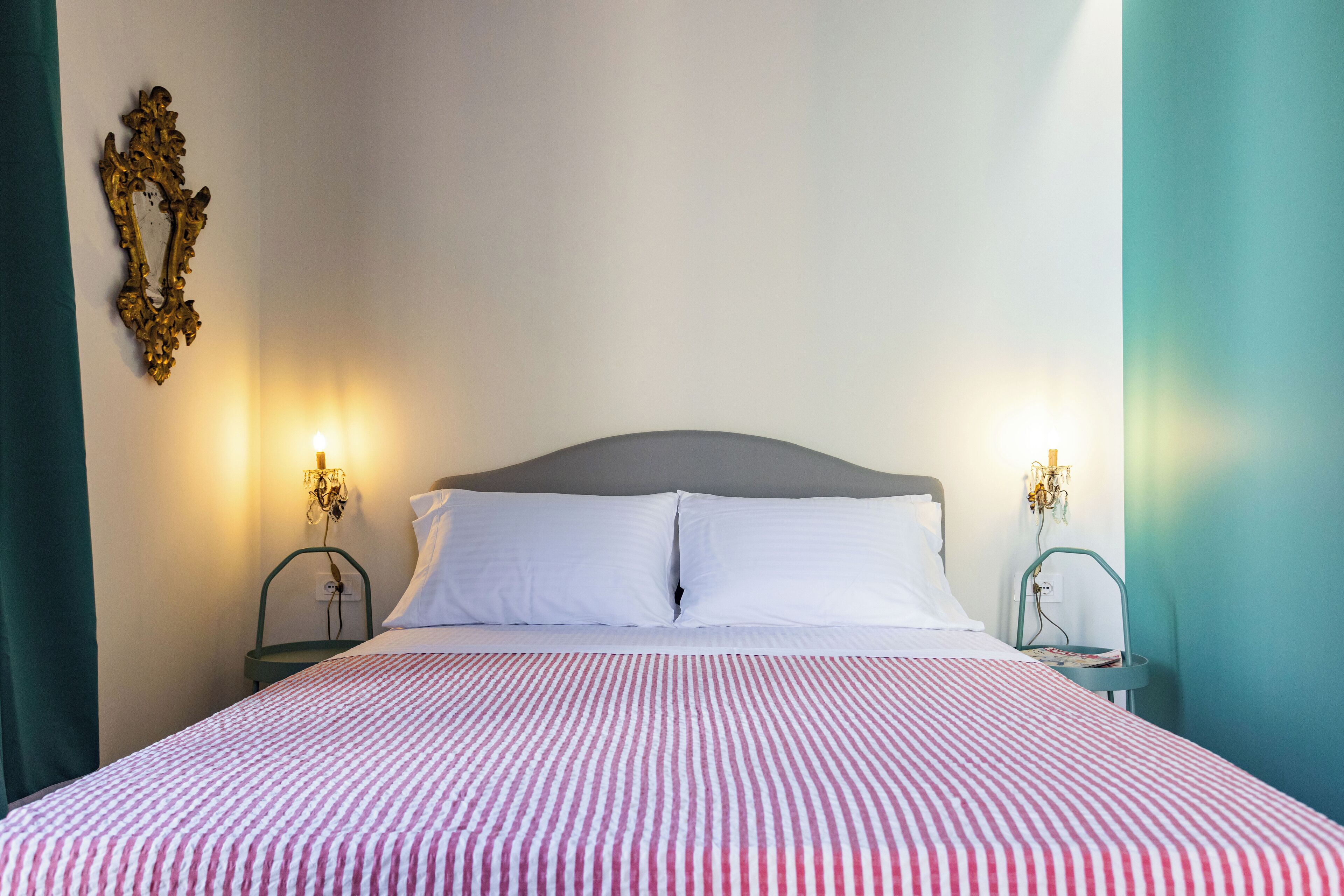 Uma cama bem arrumada com colcha listrada, duas mesas de cabeceira com abajures e um espelho decorativo na parede.