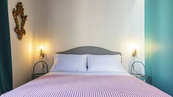 Uma cama bem arrumada com colcha listrada, duas mesas de cabeceira com abajures e um espelho decorativo na parede.