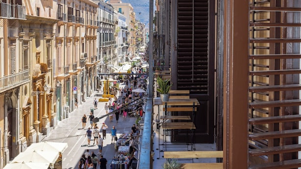 Eine belebte Straße mit Geschäften und Cafés, ein Fußweg und Häuser mit Balkonen.