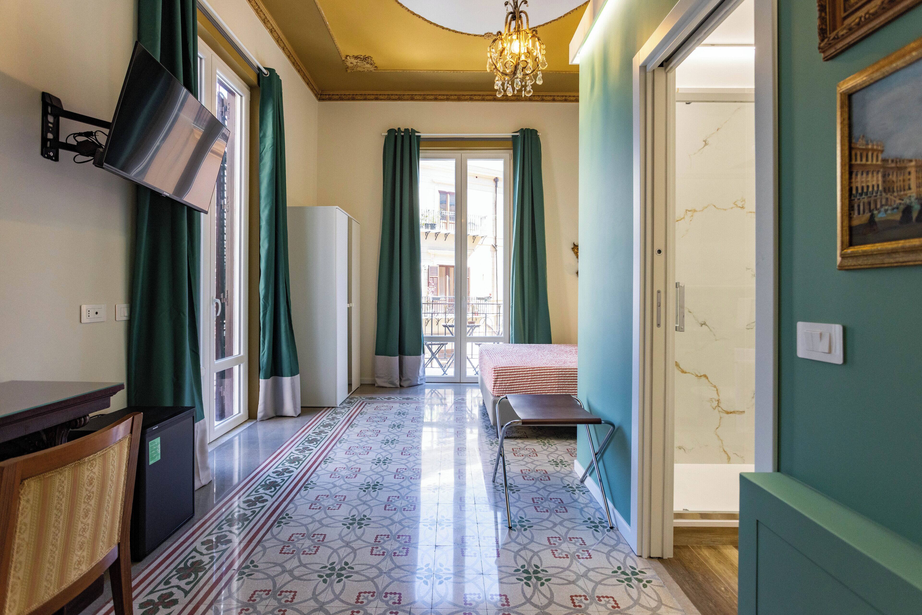 Une chambre d’hôtel avec un lit, un bureau, une chaise, un téléviseur fixé au mur et un sol à motifs.