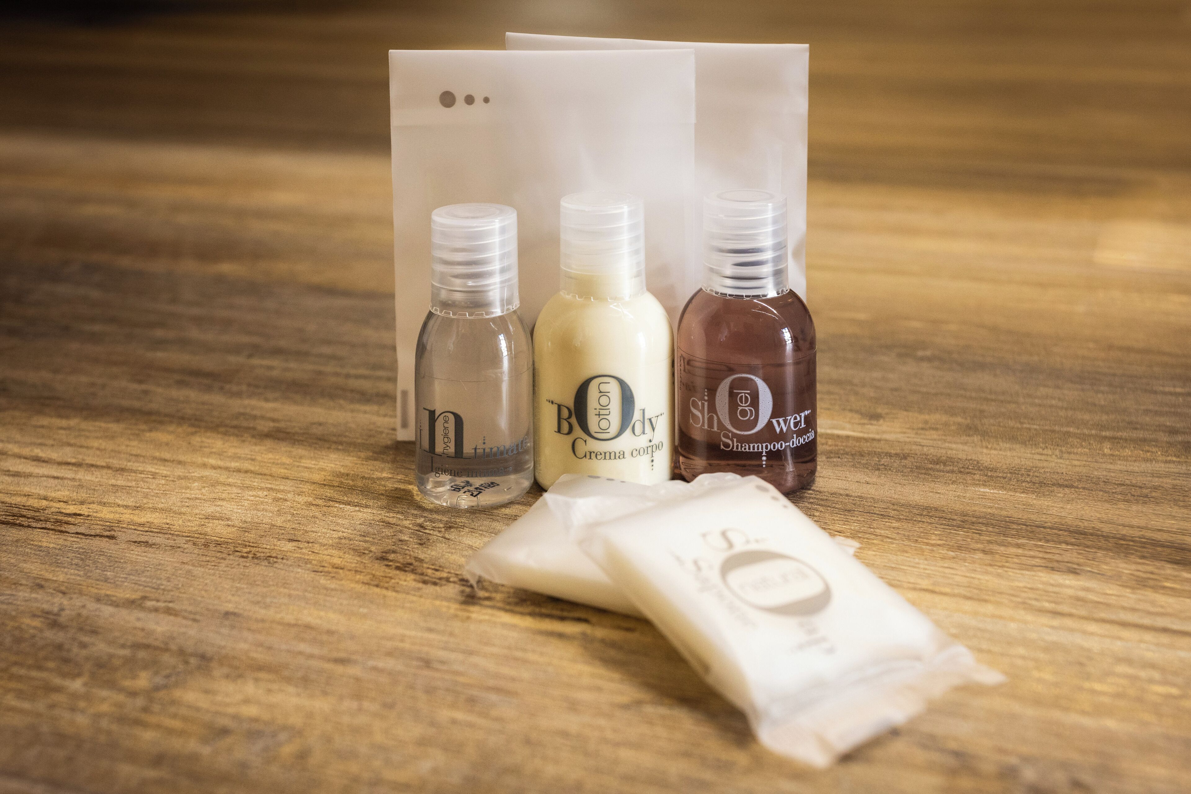Three bottles of lotion and a packet of soap on a wooden surface.