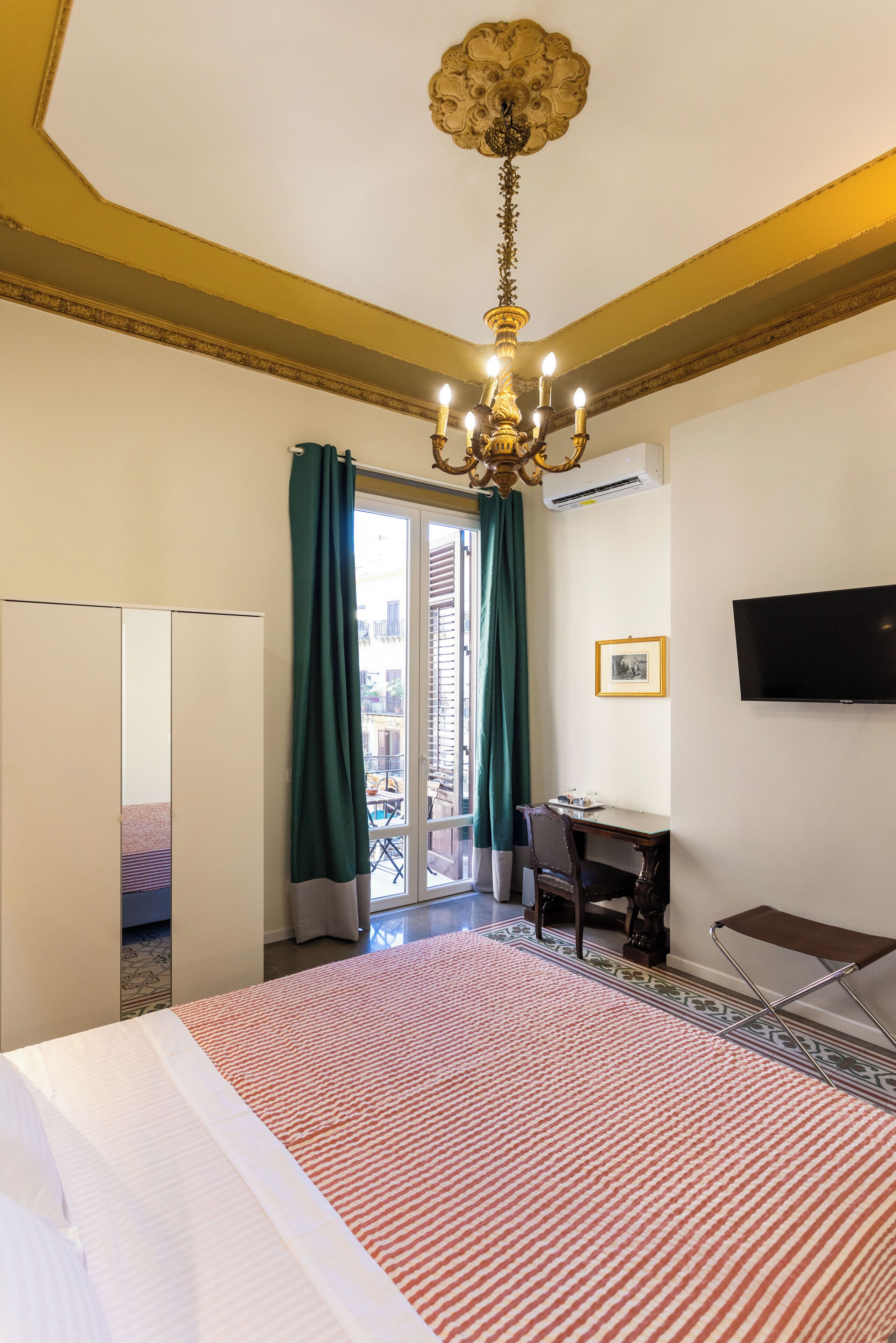 Une chambre d’hôtel équipée d’un lit, d’un bureau, d’une chaise, d’une télévision et d’un balcon avec des rideaux.