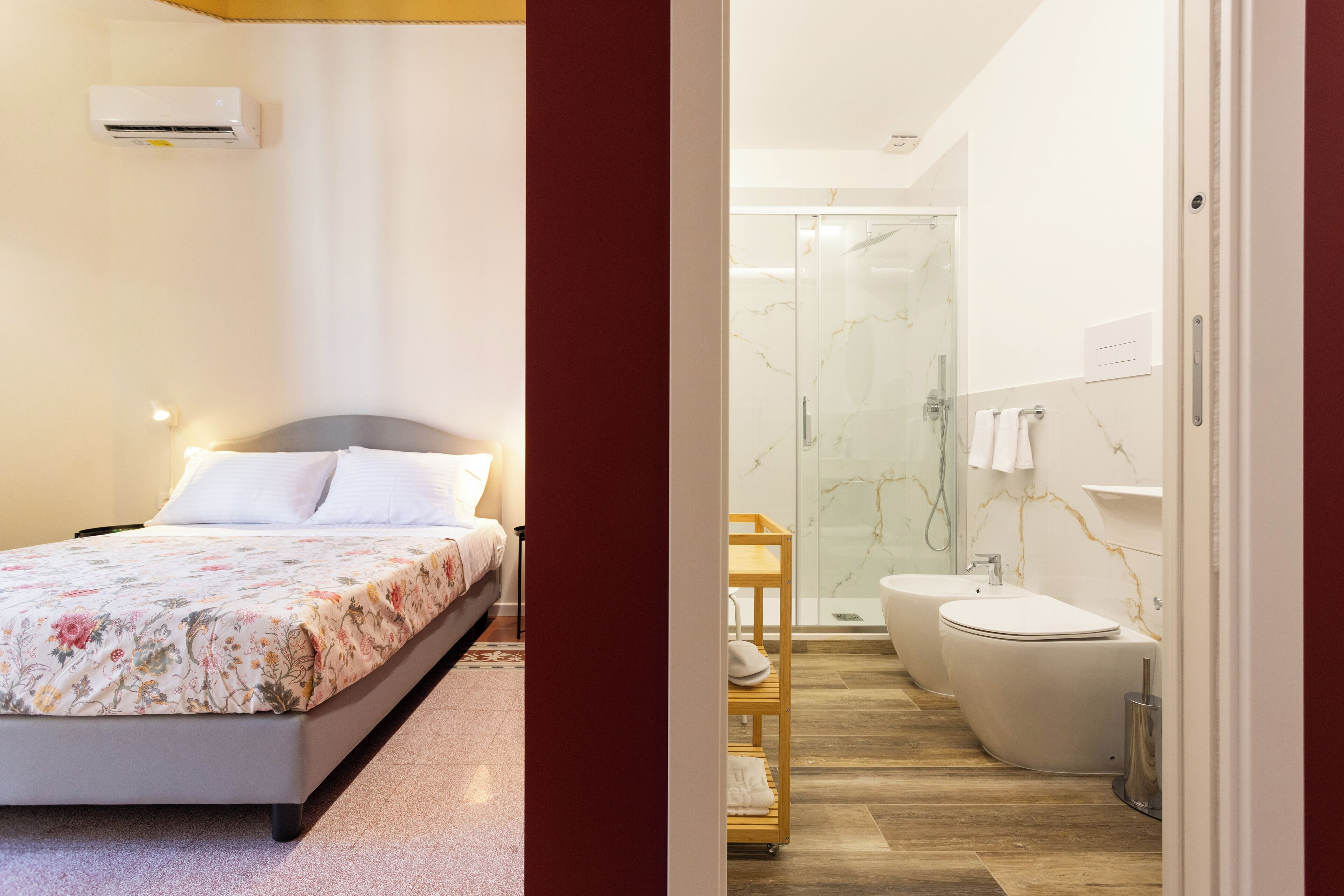 A bedroom with a bed, bedside table, and an air conditioner. The bathroom includes a shower, toilet, and sink.