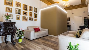 Ein Wohnzimmer mit einer Couch, einem Couchtisch und einer Topfpflanze. An den Wänden hängen Bilder in Rahmen und eine Chandelierleuchter ist angebracht.