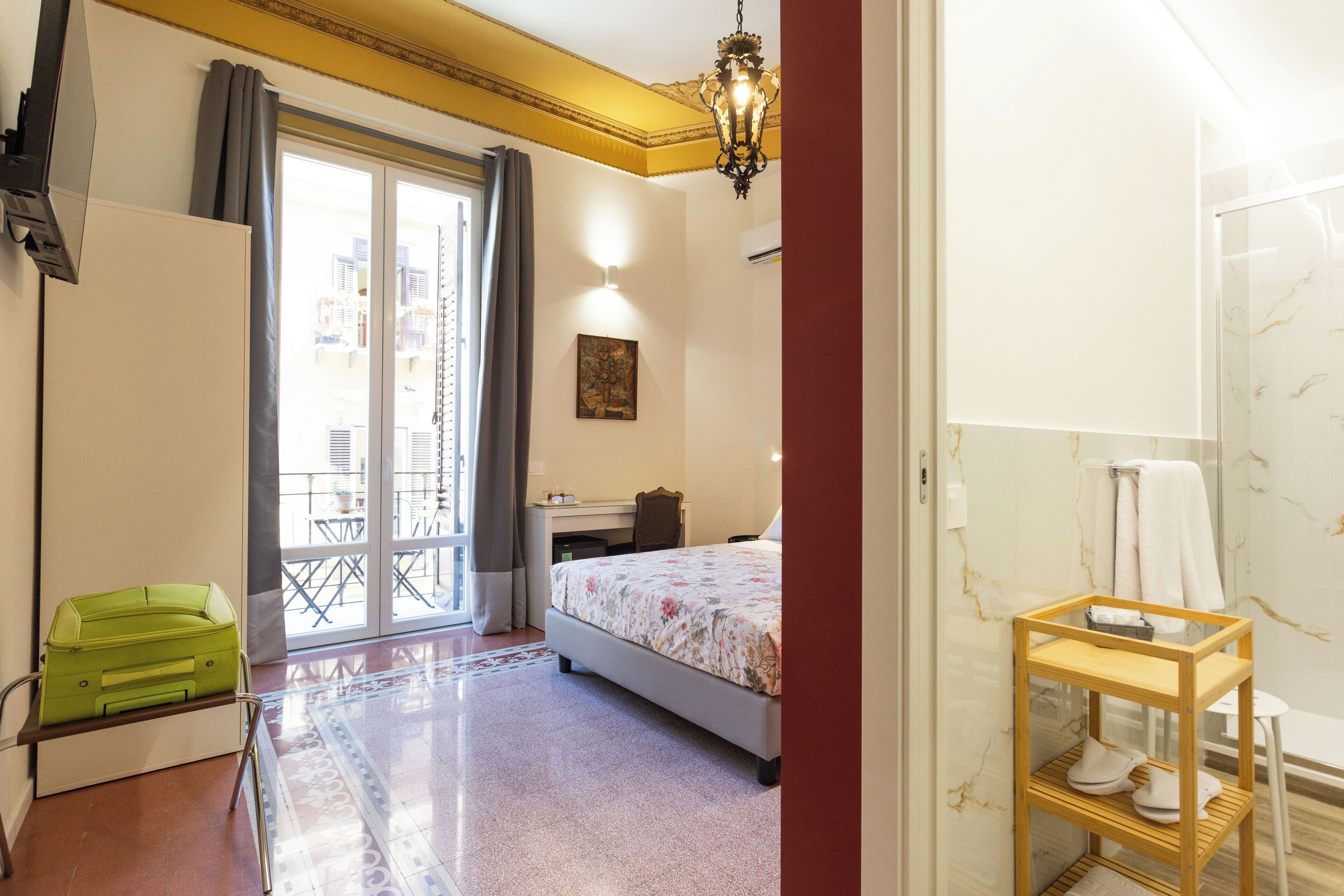 A hotel room with a bed, a desk, a chair, a suitcase, and a bathroom with a mirror and towel rack.