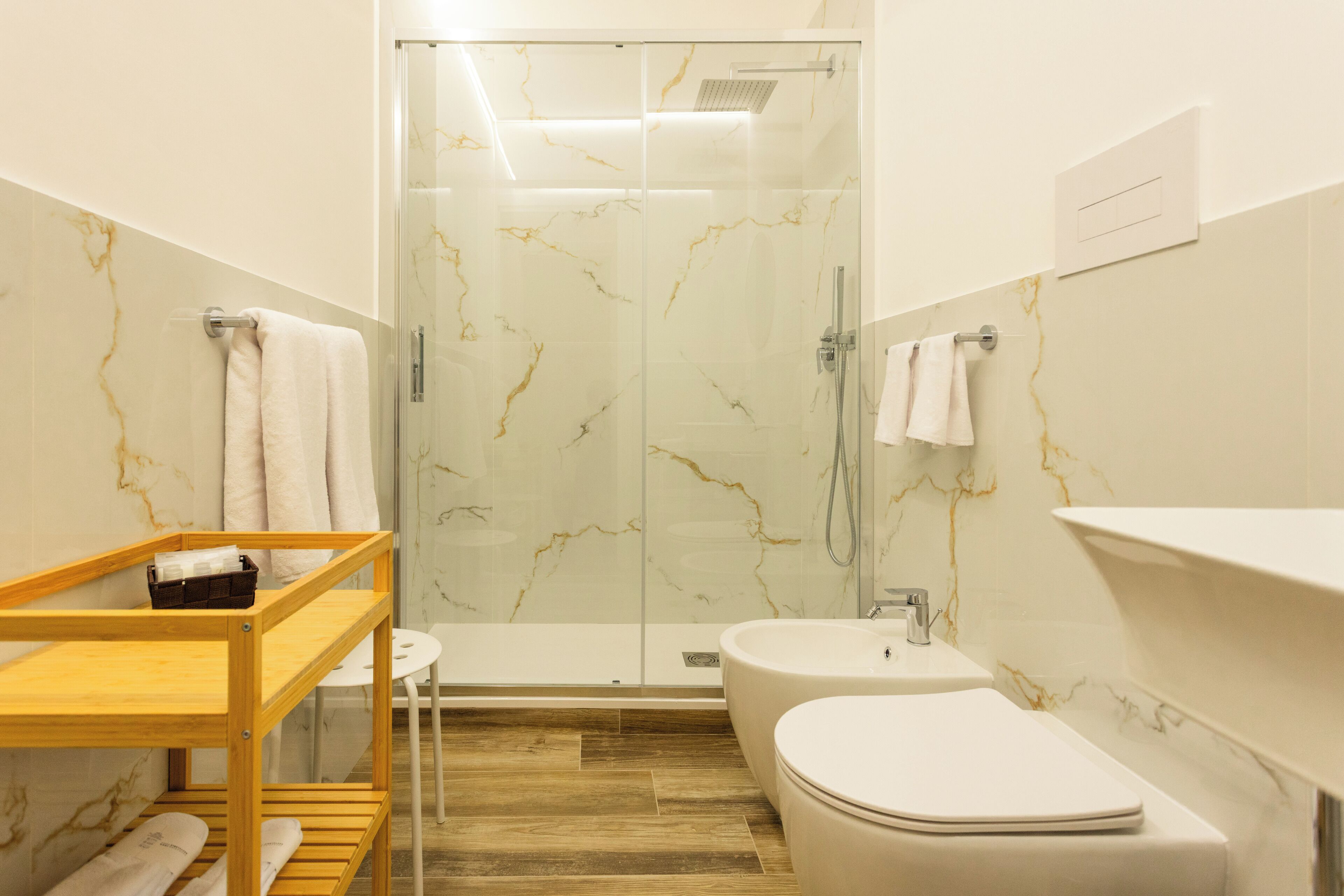 Un bany modern amb dutxa tancada amb vidre, una petita estant de fusta, un lavabo blanc i un vàter.