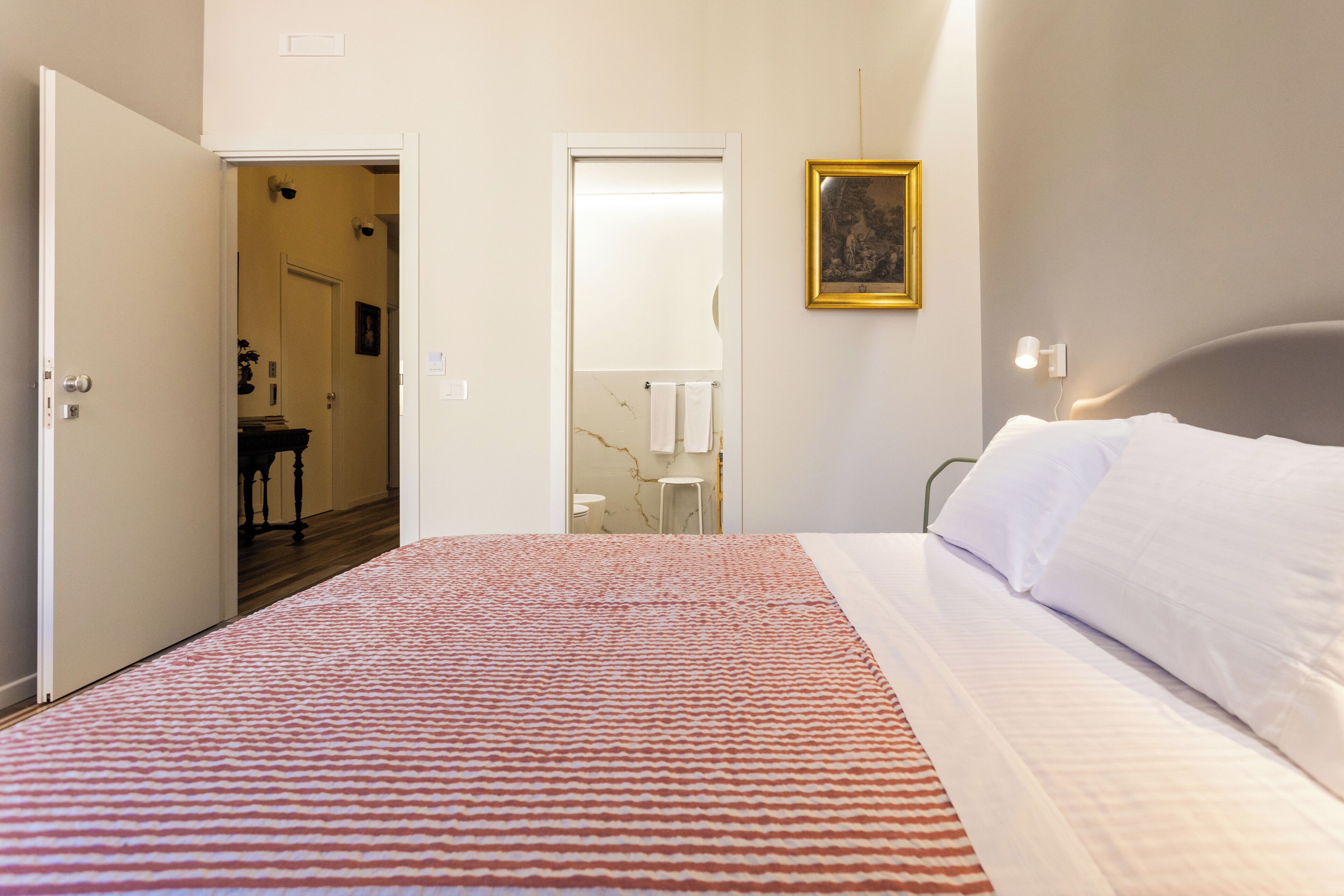 Une chambre avec un lit, une porte donnant sur une salle de bain et un couloir.