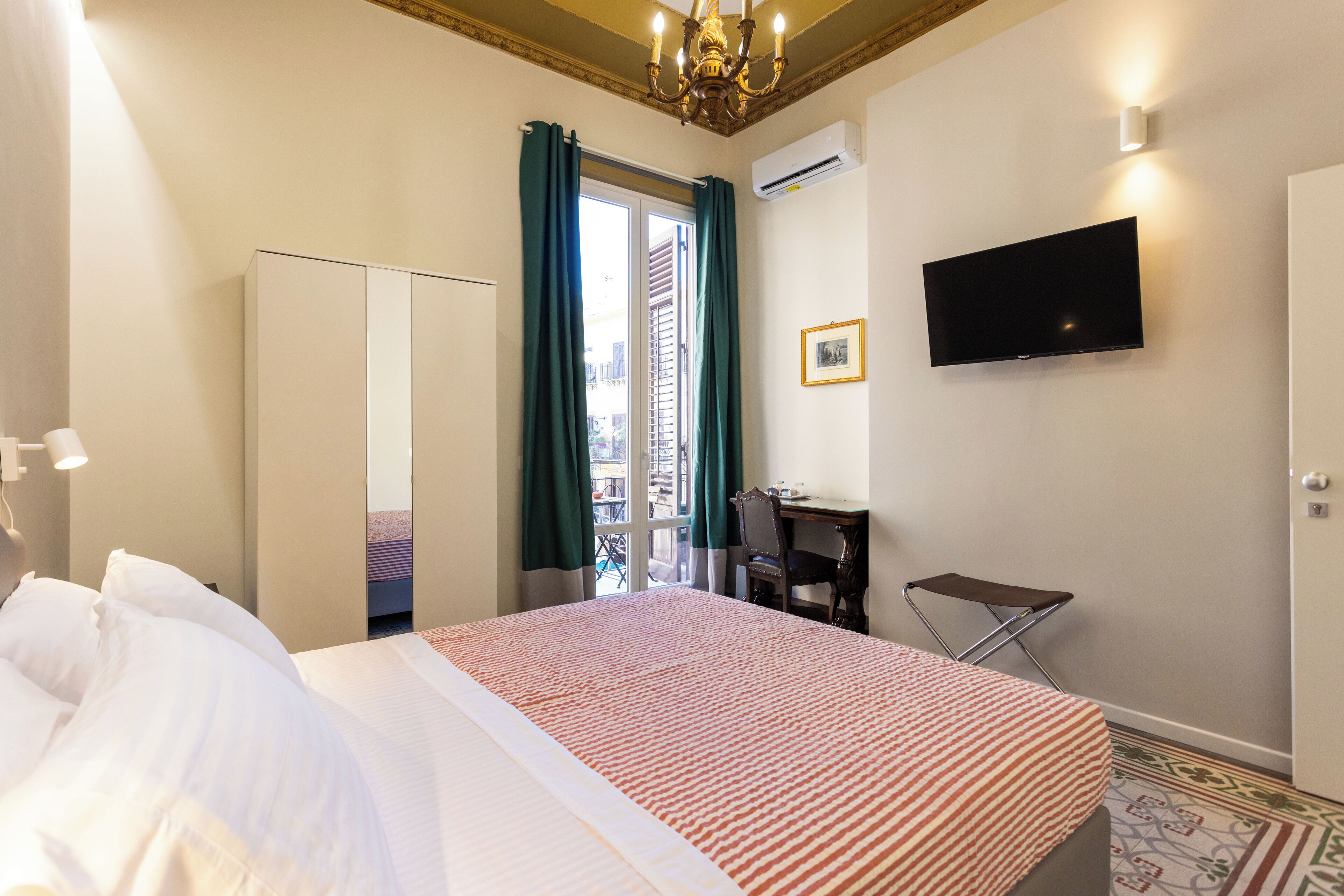Quarto de hotel com uma cama, uma escrivaninha, uma cadeira, uma televisão e uma janela com cortinas.