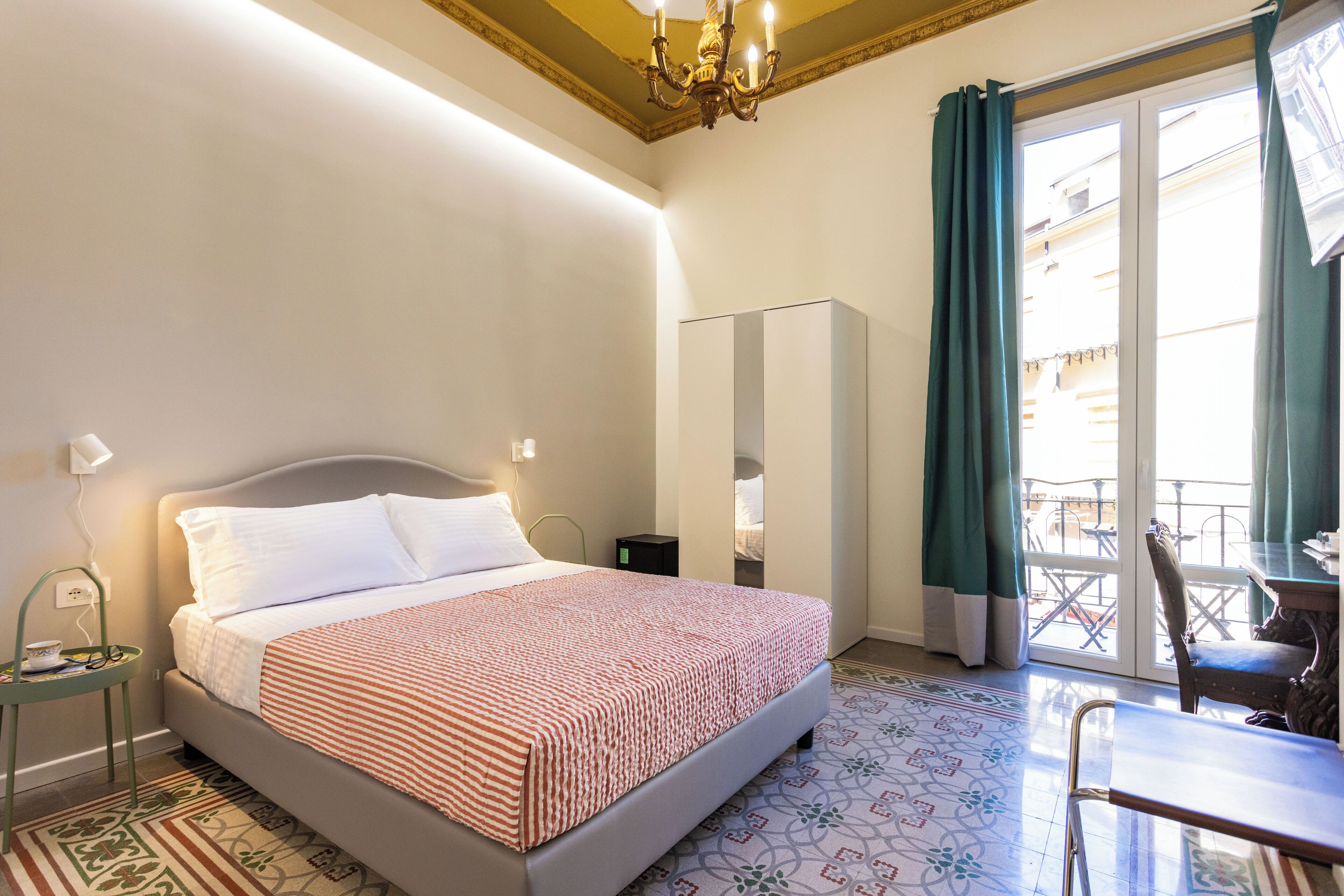 Una camera d'albergo con un letto, un tavolino, una sedia, uno specchio e un balcone con vista.