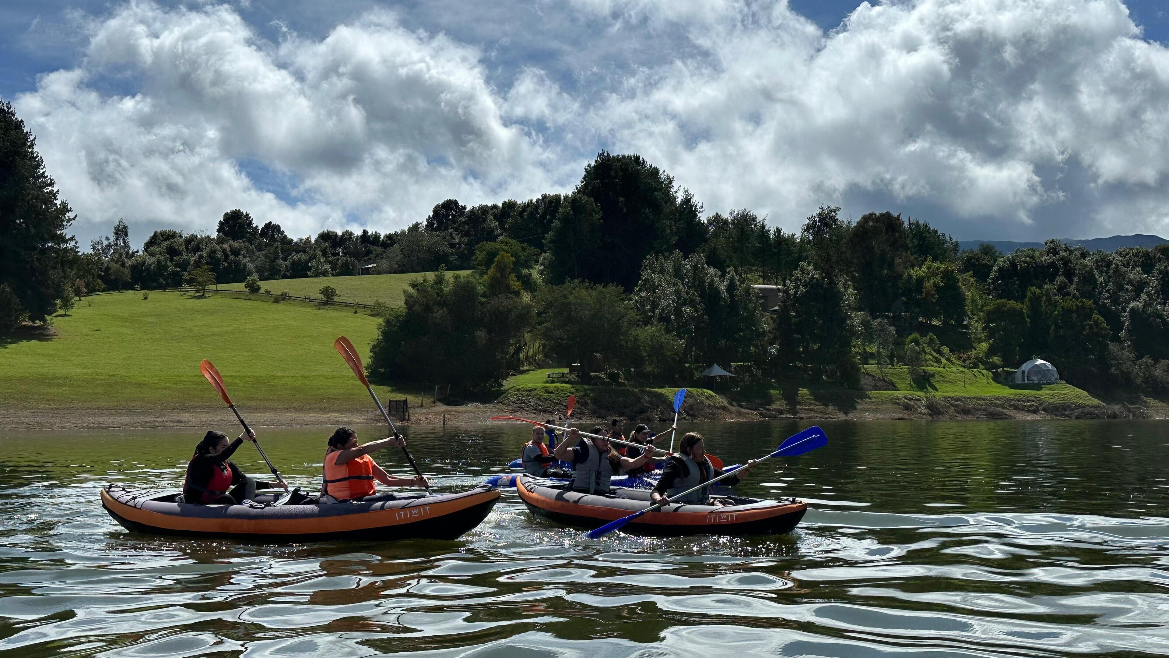 A group of people kayaking on a calm lake surrounded by lush greenery and hills.