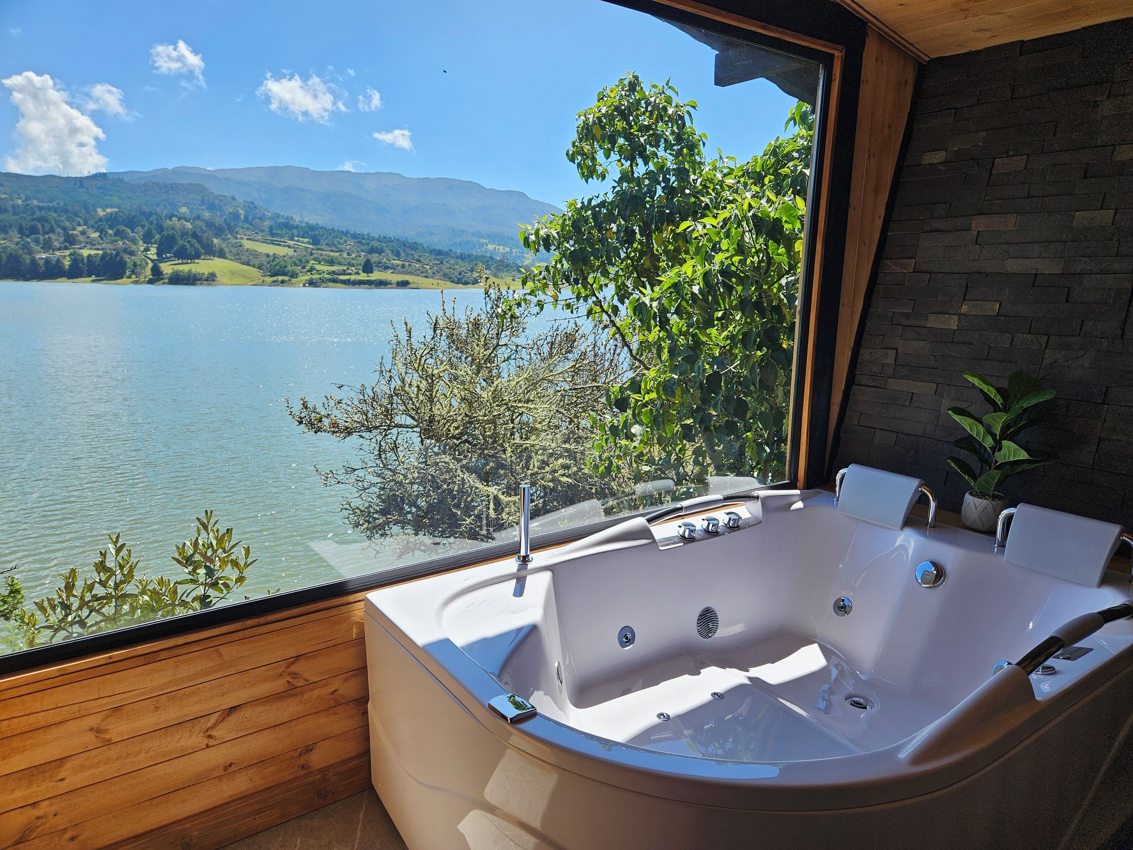 A modern bathroom with a large bathtub, a wooden floor, and a view of a lake and mountains.