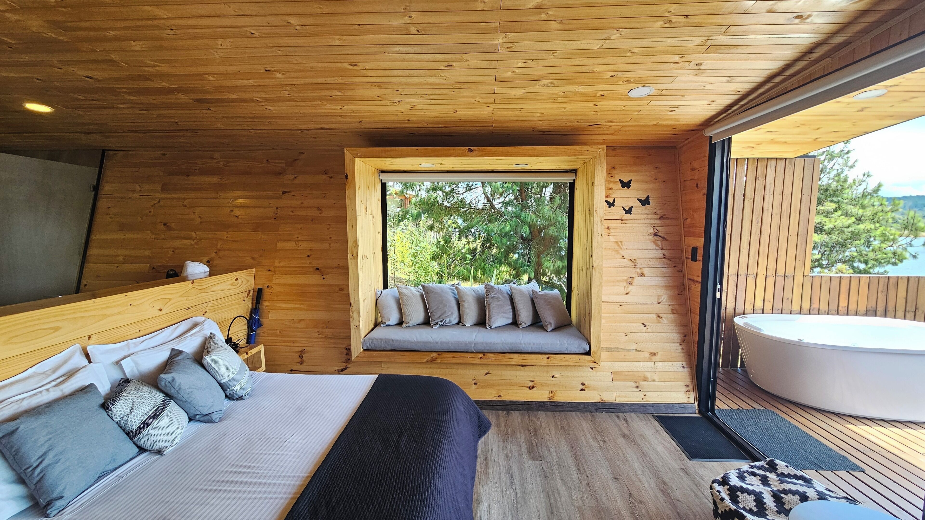 A wooden cabin bedroom with a bed, a window seat with cushions, and a hot tub.