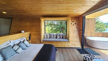 A wooden cabin bedroom with a bed, a window seat with cushions, and a hot tub.