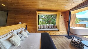 A wooden cabin bedroom with a large bed, a window seat with cushions, and a view of the outdoors. - NAQUA  (Chocontá)
