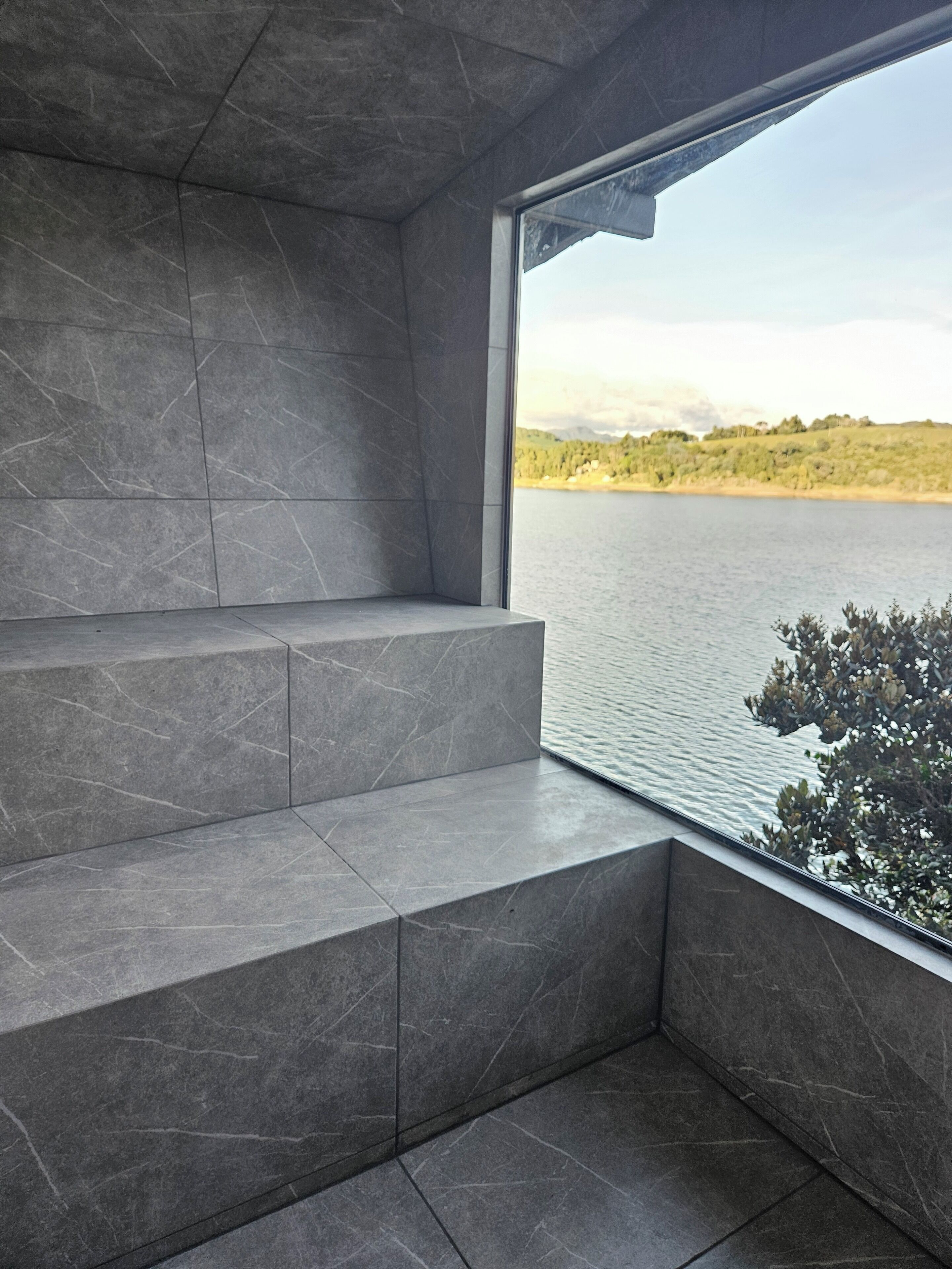A modern interior with grey tiled walls and a large window overlooking a lake.