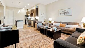 Ein modernes Wohnzimmer mit Sofa, Couchtisch und Essbereich, im Hintergrund eine Küche.