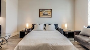 Ein Schlafzimmer mit einem großen Bett, zwei Nachttischen mit Lampen, einem Sofa und einem Wandbild.