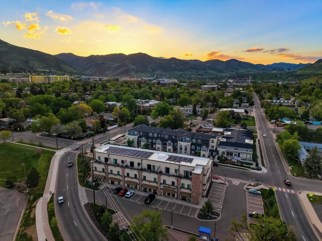 An aerial view of a town with a prominent building featuring a solar panel roof, surrounded by roads and greenery.