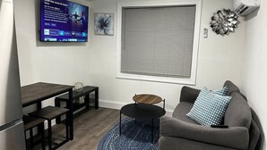 Een ruimtelijke zithoek met een eethoek, een bank, een klein rond tafeltje en een televisie aan de muur.