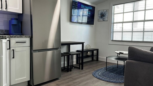 Een moderne keuken met een roestvrijstalen koelkast, een eettafel met twee stoelen, een klein rond tafeltje en een grijze bank.